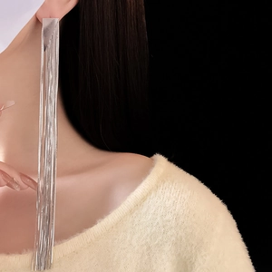 Model wearing long silver tassel earrings with multiple metal chains draping to the shoulder