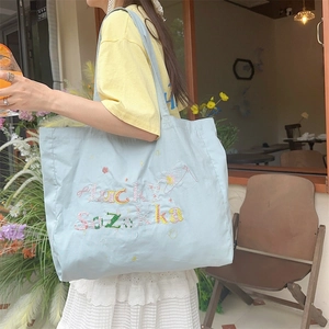 Détail d'un sac cabas en toile bleu clair avec broderie colorée porte-bonheur