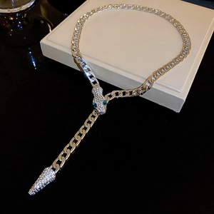 Close-up of silver snake necklace with rhinestones and green eyes on a beige display box