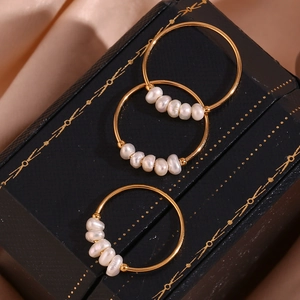 Detail of gold hoop earrings with white baroque pearls on a peach silk fabric background