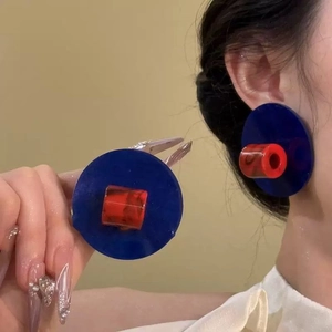 Détail de boucles d'oreilles géométriques rouge et bleu portées par un modèle