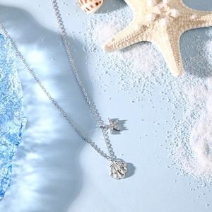 Detailed shot of S925 silver necklace with shell and starfish pendants on white sand