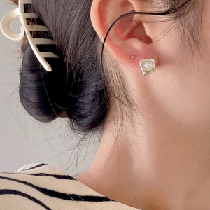 Close-up of minimalist pearl stud earrings on model with elegant square setting details