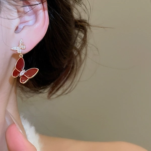 Detail of elegant gold butterfly earrings with red enamel and zircon on model's ear
