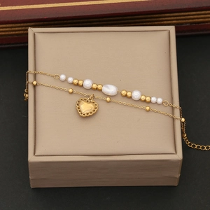 Détail d'un bracelet double chaîne doré avec pendentif cœur et perles sur écrin à bijoux