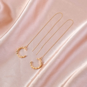 Orecchini a catena in oro con pendente a forma di C su sfondo in seta champagne