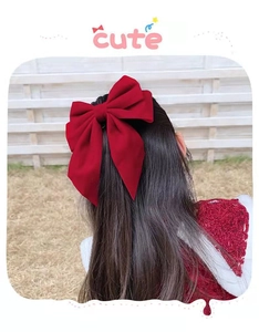 Close-up of a large red bow hair clip worn on the back of a girl head outdoors