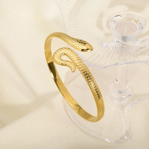 Detail of gold snake-shaped bangle with scale texture hanging on a glass rim