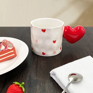 Detail of a ceramic mug with red heart patterns and a unique heart-shaped handle on a wooden table