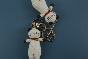 Close-up of handmade crochet cat keychains with red scarves and golden bells on blue background