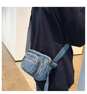 Detail of blue denim crossbody bag featuring multi-layer storage and metal zippers