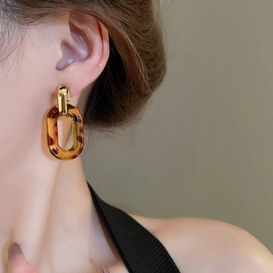Close-up of amber resin chain earrings with gold metal accents worn on a female model