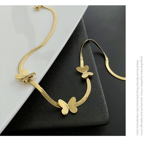Détail des pendentifs papillon dorés sur un collier à chaîne serpent lisse