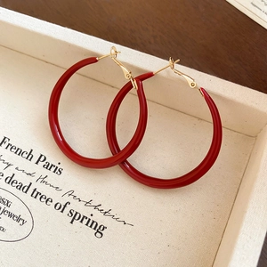 Close-up of vintage red enamel hoop earrings with gold needles on a cream fabric box