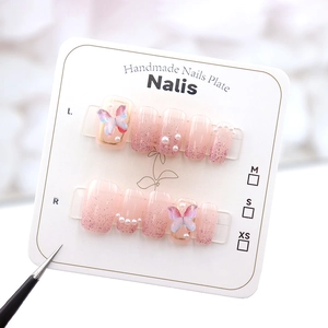 Detail of handmade press-on nails with pink gradient, 3D butterfly, and pearl accents