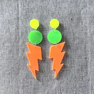 Detail of neon acrylic earrings with fluorescent lightning bolt charms on linen background