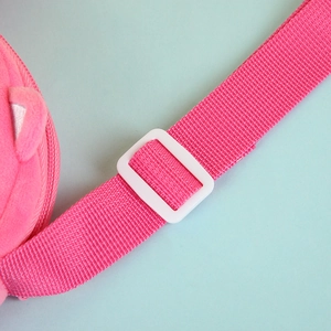 Close-up of pink woven strap and white plastic adjustment buckle on plush owl crossbody bag