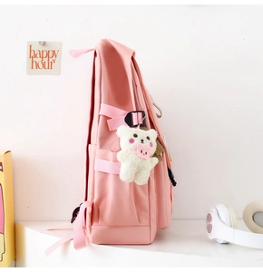 Side view of pink nylon school backpack with side straps and cute plush bear charm