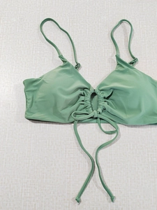 Detail of sage green bikini top featuring central ruching and adjustable tie strings