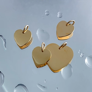 Polished gold stainless steel heart pendants on a reflective water drop surface