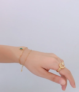 Close-up of double-layer gold chain bracelet with emerald green geometric pendant