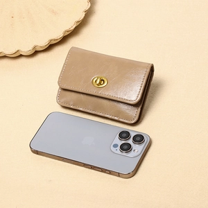 Detail der khakifarbene Mini-Geldbörse aus Leder mit Drehverschluss neben einem Smartphone