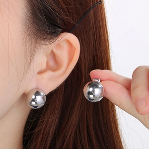 Close-up of minimalist silver spherical stud earrings on model for size reference