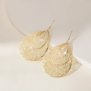 Detailed close-up of triple-layered golden teardrop earrings with intricate filigree patterns