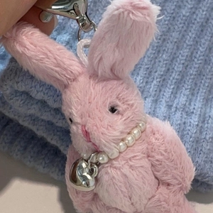 Cute pink plush bunny keychain with pearl necklace and heart pendant on blue knit background