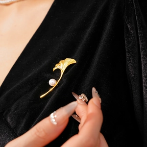 Detail of gold ginkgo leaf brooch with pearl on black velvet fabric and hand model