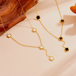 Collier chic en Y doré avec pendentifs carrés noirs et blancs sur fond de bois