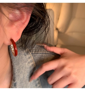 Close-up of model wearing C-shaped earrings with red enamel and sparkling zircons