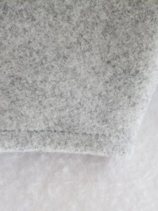 Macro shot of grey wool fabric texture with detailed single needle stitching on the edge