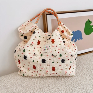 Detail of Christmas themed cream puffer bag with drawstring and woven handles on soft rug