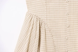 Detailed close-up of beige plaid dress featuring covered buttons and waist pleats