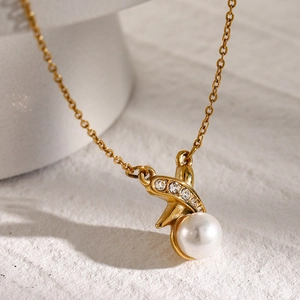Macro shot of a gold X-shaped pendant with three small diamonds and a round white pearl