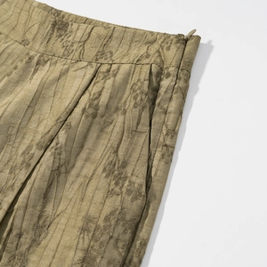 Detailed close-up of olive green pleated pants with hidden zipper and side seam pocket