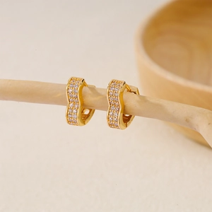 Macro detail of wave-shaped gold earrings with paved cubic zirconia on a branch