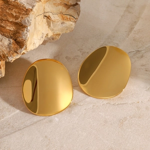 Macro shot of gold-plated pebble-shaped geometric stud earrings on marble surface