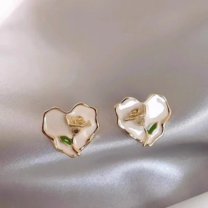 Macro shot of gold heart earrings with white enamel and rose detail on grey silk