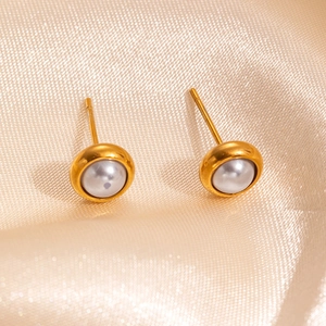 Close-up of elegant gold pearl stud earrings on a luxurious light gold satin background