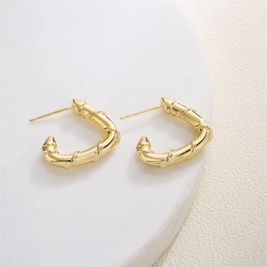 Golden bamboo texture geometric hoop earrings on a marble stone and beige fabric
