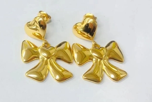 Detailed macro view of 14K gold plated bow and heart drop earrings with a mirror finish