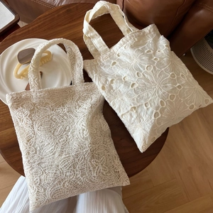 Close-up of two white lace tote bags with vintage embroidery on a dark wooden table