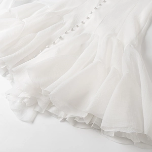 Close-up of elegant tiered ruffles and fabric-covered buttons on a white dress