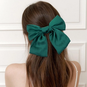Detail showing a large dark green satin bow hair clip worn on the back of the head