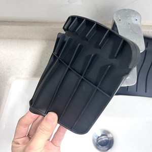 Close-up of black silicone faucet drying mat being held over a white bathroom sink