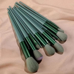 Flat lay of 13 professional makeup brushes with green handles on soft pink silk background