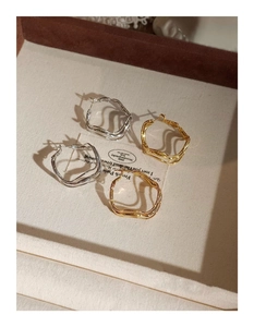 Detail view of irregular wavy gold and silver hoop earrings on beige fabric display