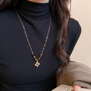 Close-up of a vintage tiger eye flower pendant necklace worn on a black turtleneck